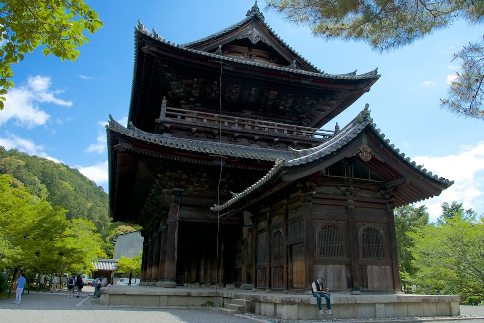 A traditional Japanese pagoda with multiple tiers and ornate roof tiles, surrounded by lush greenery and trees.