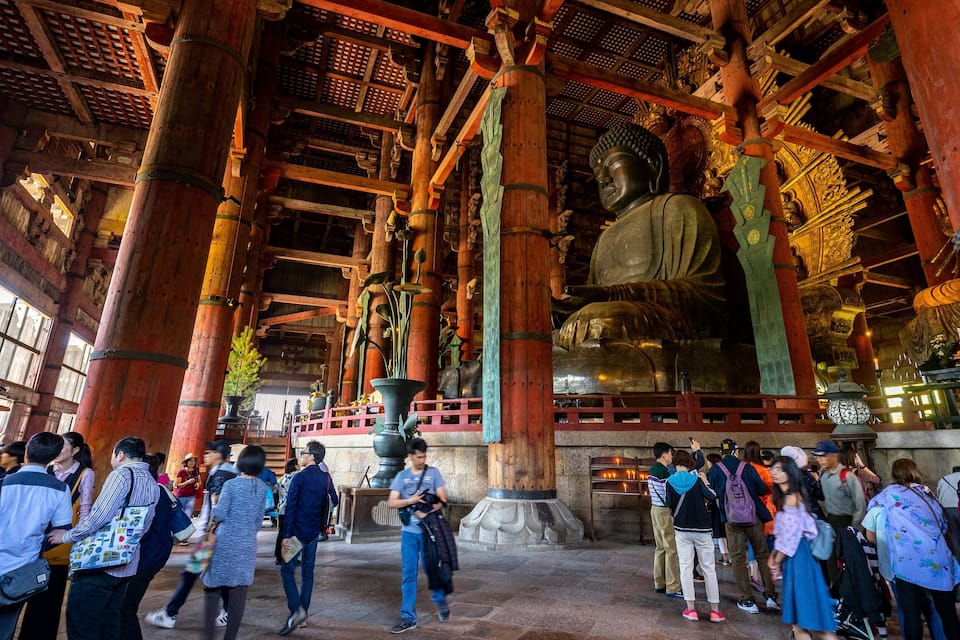 A large Buddha statue in a temple with a crowd of people around it.