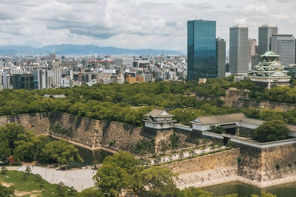 A cityscape with modern skyscrapers and traditional Japanese castle ruins.