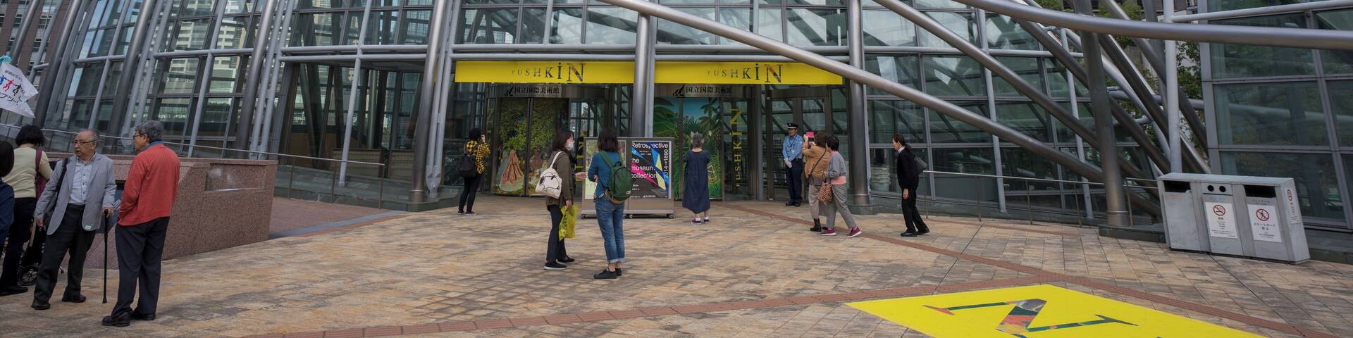 A modern glass building with a curved metal framework and a yellow entrance sign.