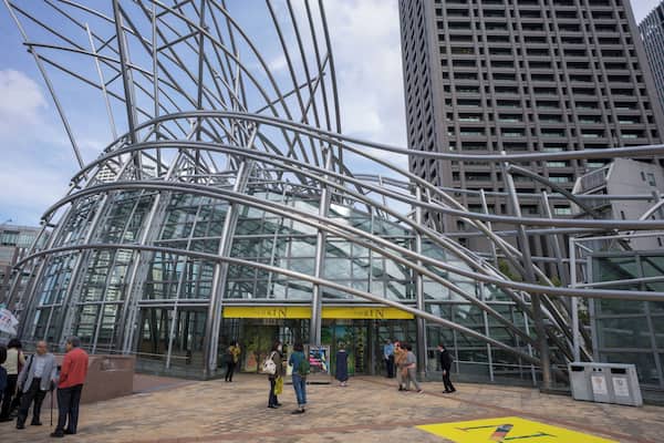 Un bâtiment moderne en verre, doté d’une structure métallique incurvée et d’une enseigne jaune à l’entrée.
