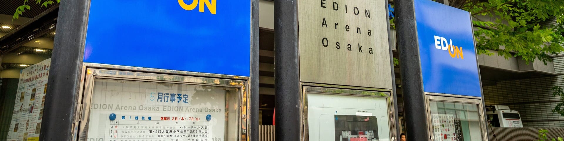 Three EDUN signs in front of a building with trees and a metal structure.