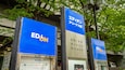Three EDUN signs in front of a building with trees and a metal structure.