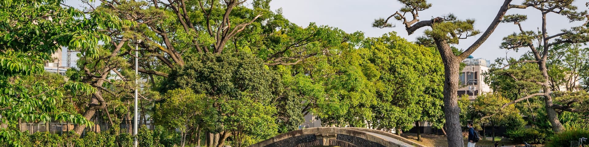 A stone bridge over a calm river, surrounded by lush greenery and trees.
