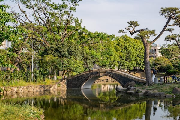 Un pont de pierre enjambant une rivière paisible, entouré d’une végétation luxuriante et d’arbres.