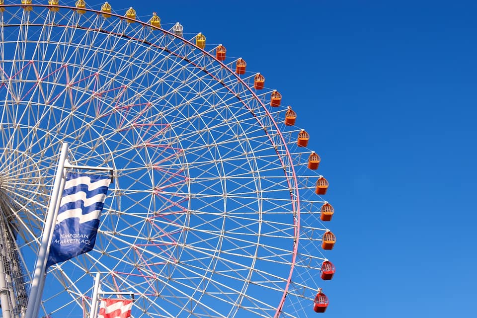 Una gran noria amb cistelles vermelles davant d'un cel blau clar.