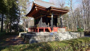 A traditional pavilion with a tiled roof, surrounded by trees and a stone pathway.