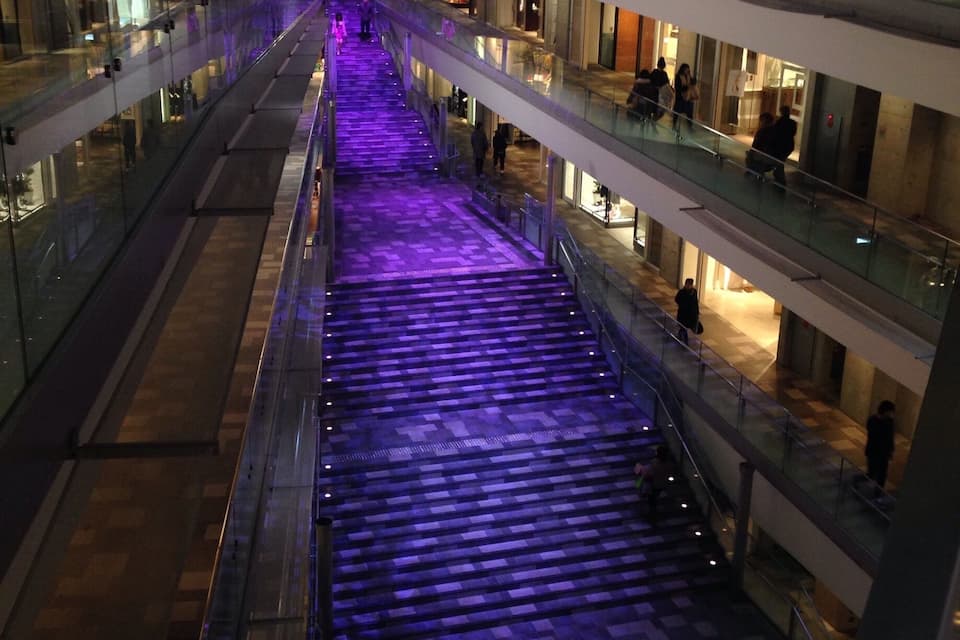 Un centro commerciale a più piani con un'escalatora centrale e un percorso illuminato di viola.