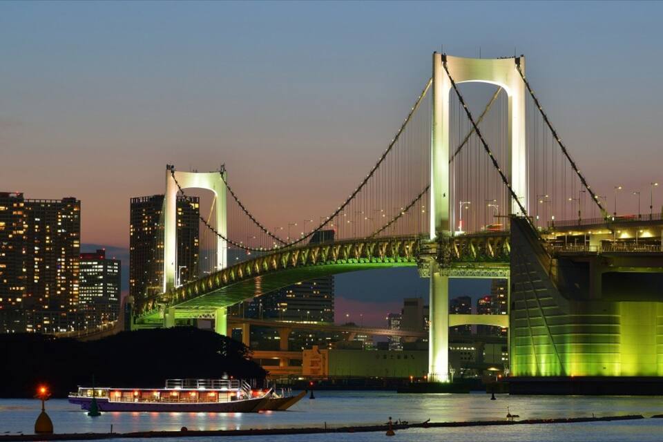 Un grand pont illuminé enjambant une étendue d’eau, avec la silhouette d’une ville en arrière-plan.