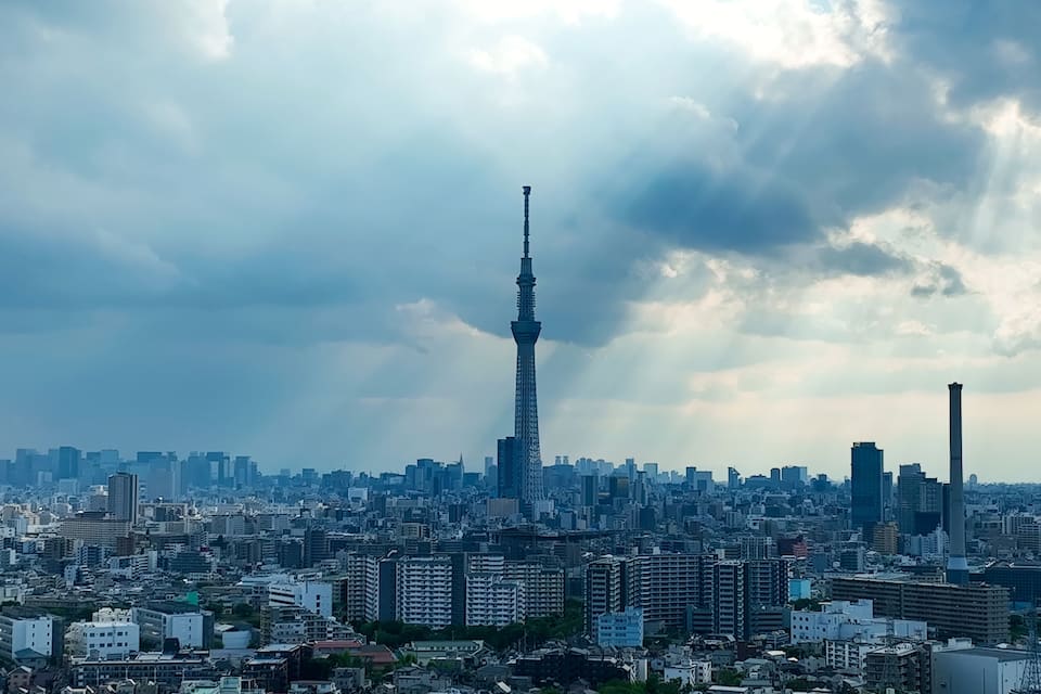 A cityscape with a prominent tower in the center, surrounded by dense urban buildings under a cloudy sky.