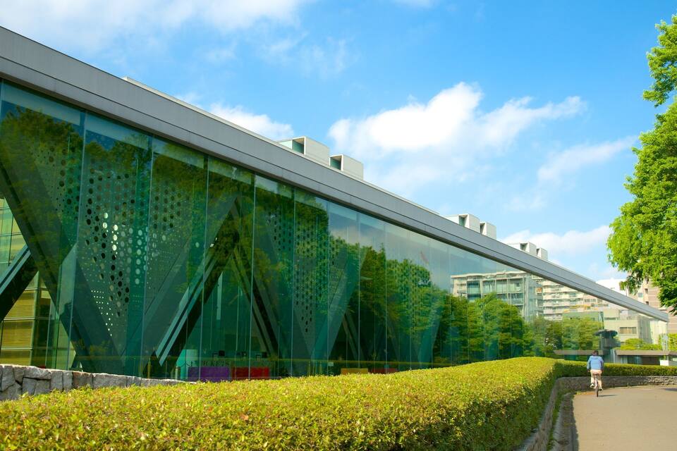 Un edificio moderno con fachada de vidrio reflectante, un jardín ajardinado y un cielo azul despejado.
