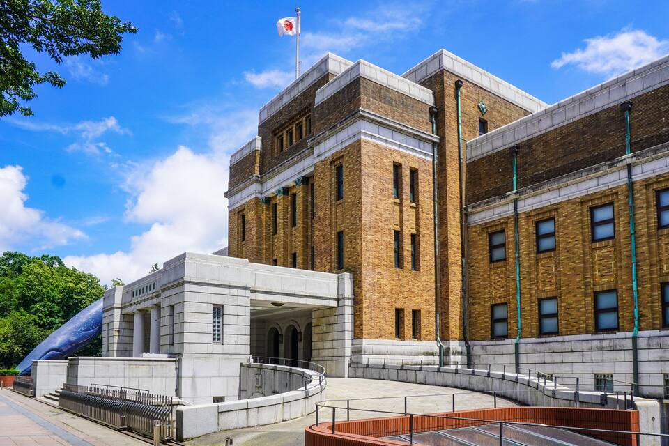 A large brick building with a flag on top, a circular plaza with a fountain, and a modern sculpture.