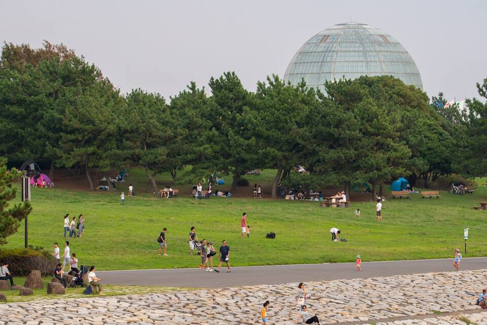 A park with a large glass dome structure, picnic areas, and a stone wall.