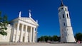 A neoclassical building with columns and statues, and a tall tower with a clock.