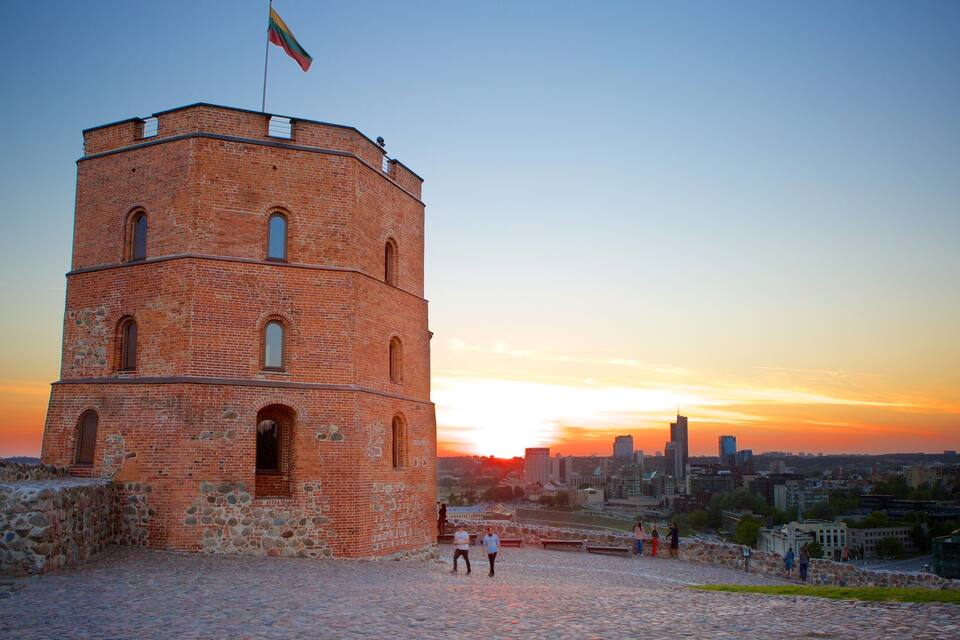 A brick tower with a flag, set against a sunset cityscape.