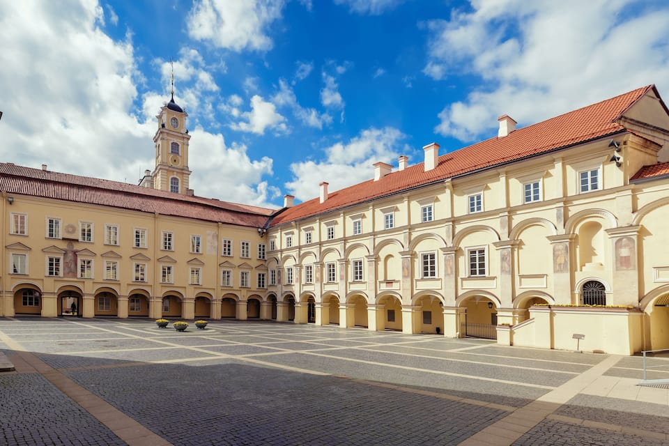 A courtyard with a clock tower, arched walkways, and a tiled roof.