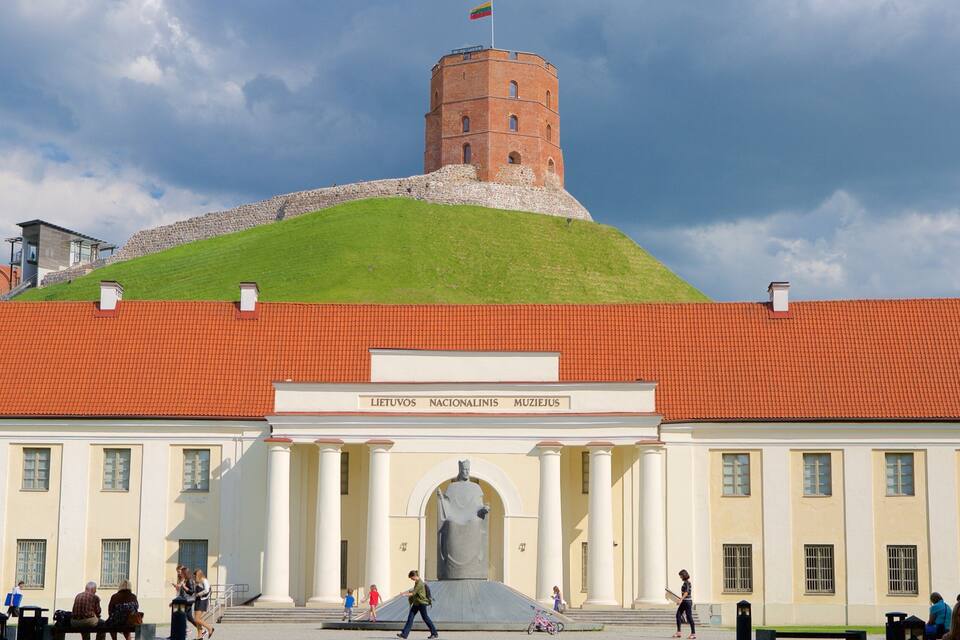A building with a red roof and a statue in front. There is a tower on a hill in the background.