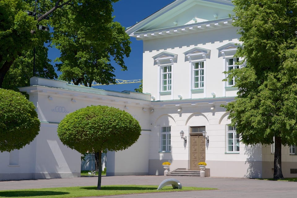 A white building with a green roof and a large tree in front.