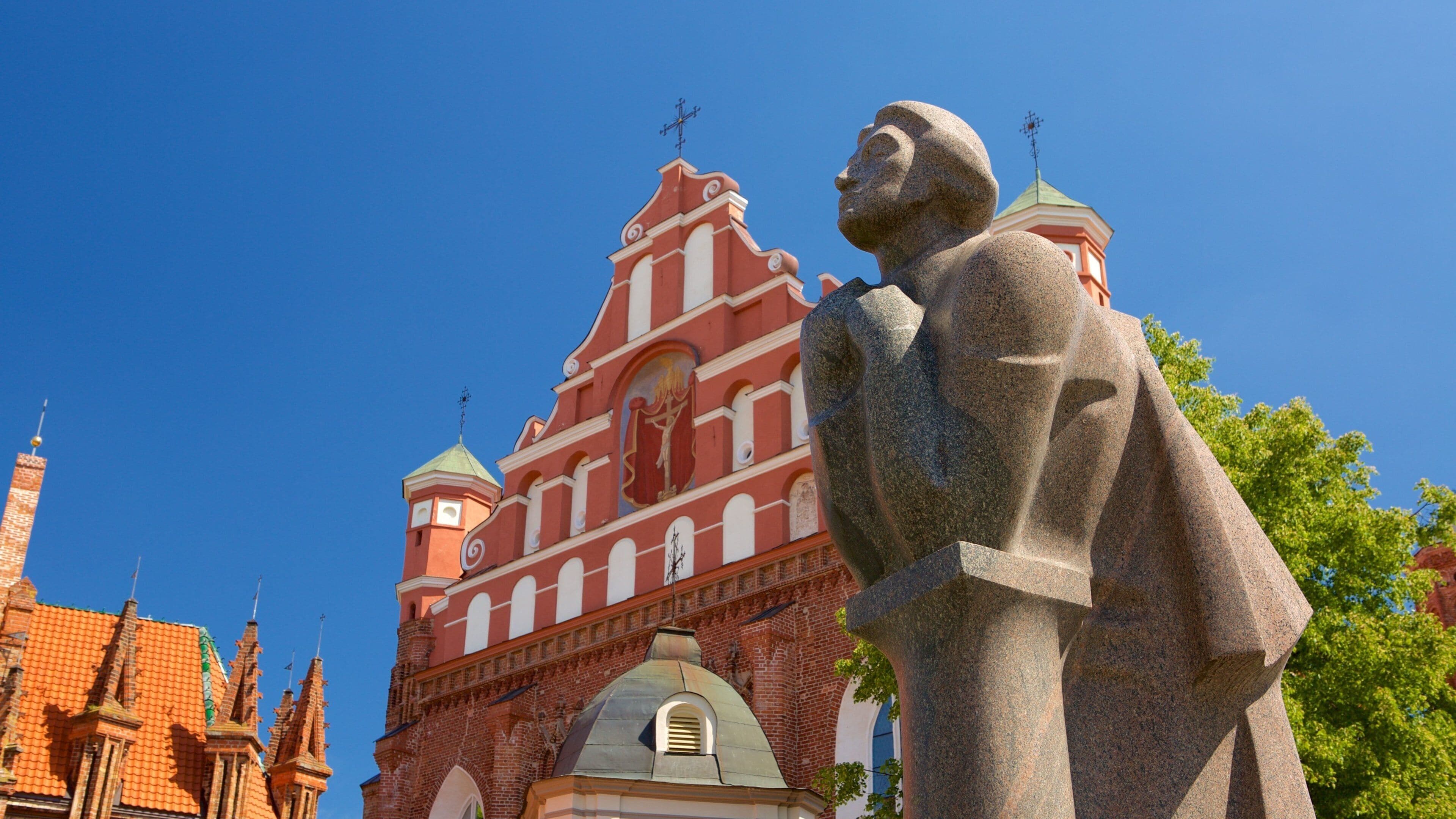 A stone statue in front of a red brick church with a green dome and a cross on top.
