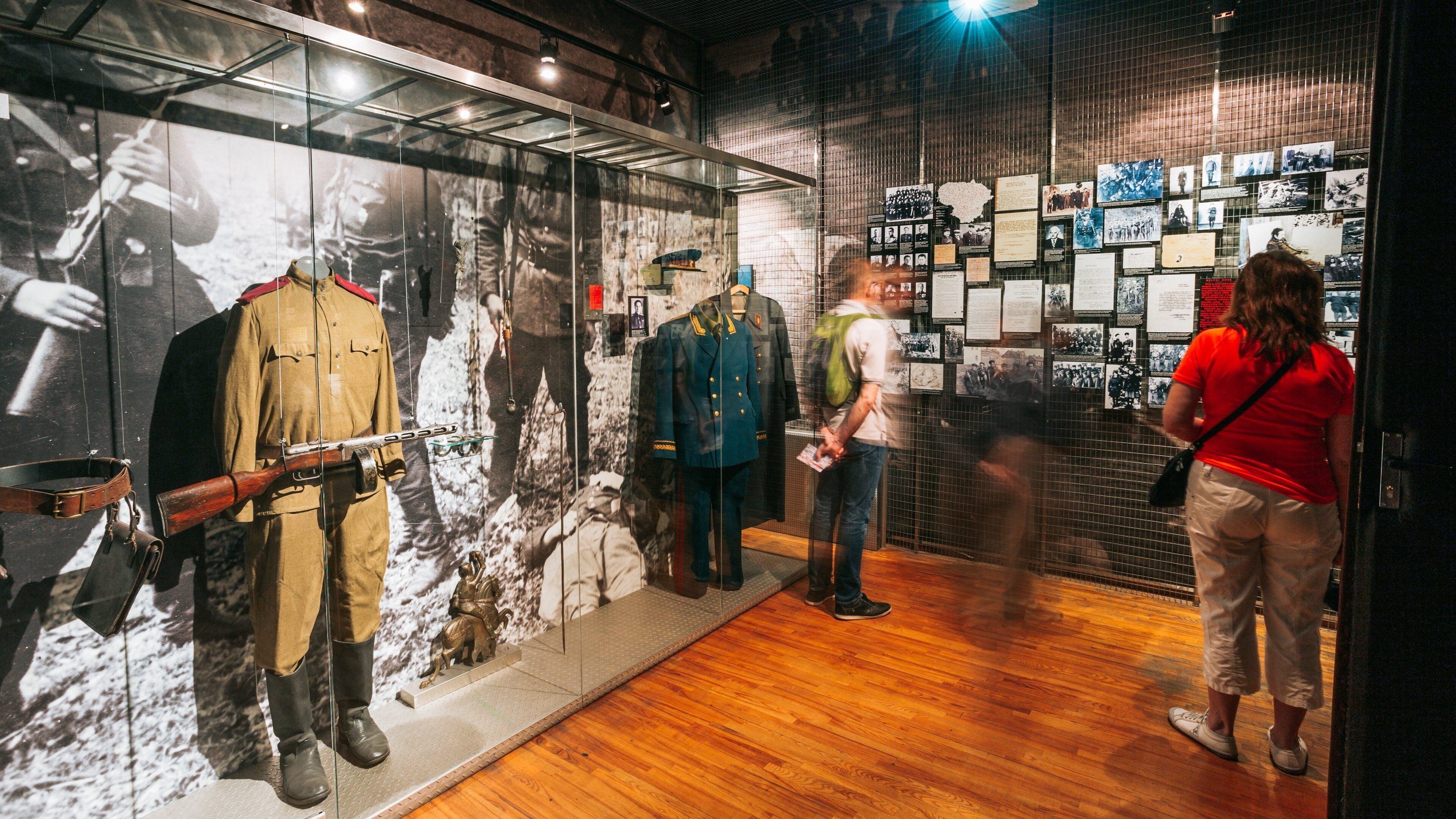 A museum exhibit with mannequins in military uniforms, a rifle, and a backdrop of historical photographs.