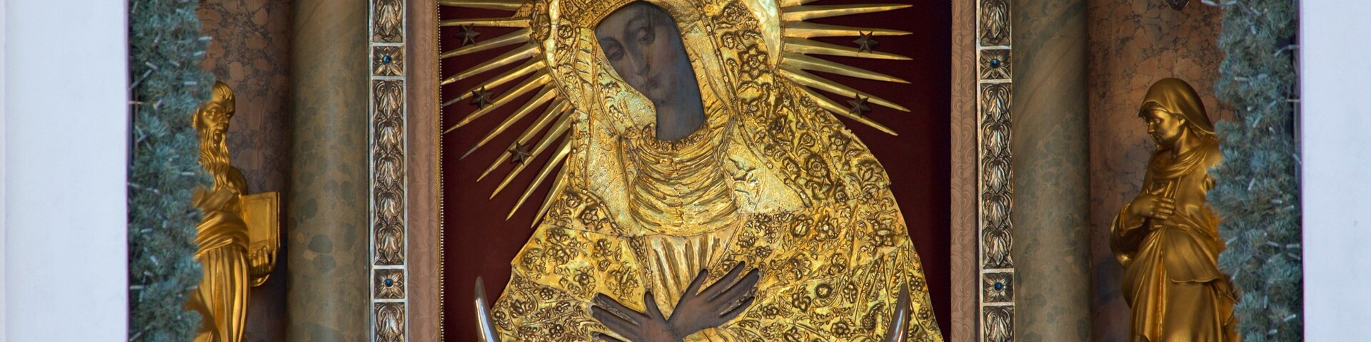 Un ícono religioso dorado con un halo, flanqueado por dos estatuas, sobre un fondo de mármol.