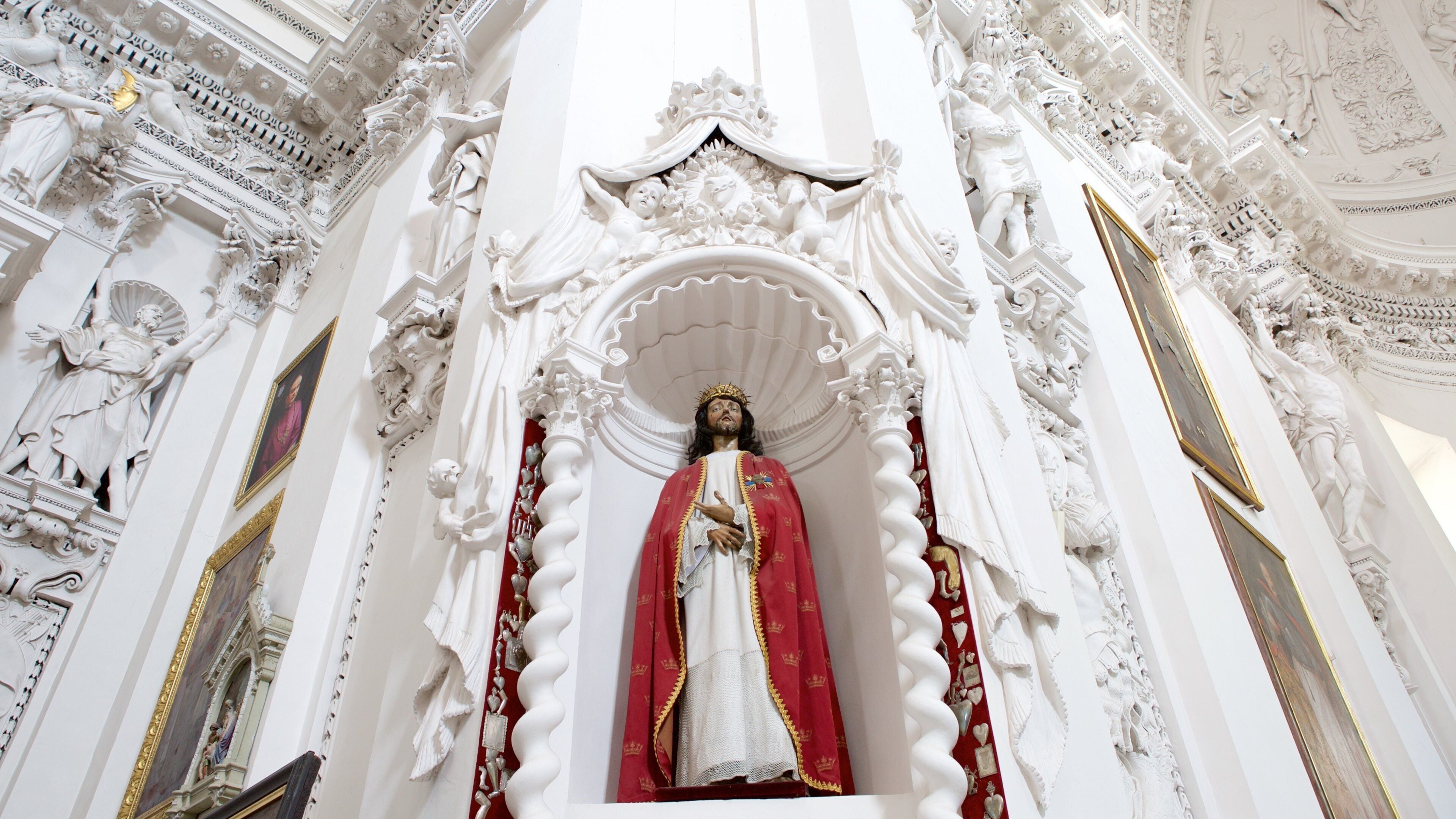 Eine Statue in einer weißen, kunstvoll verzierten Kirche mit aufwendigen Schnitzereien und einer roten und goldenen Robe.