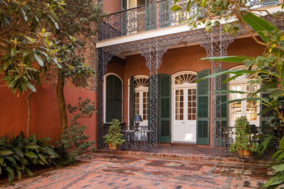 A courtyard with a brick floor, green shutters, and a balcony with wrought iron railings.