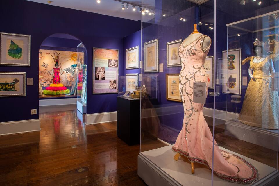 Une galerie d’art où sont exposées des œuvres encadrées et des mannequins portant des robes.