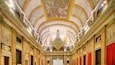 A grand hall with ornate ceilings, columns, and a central chandelier.
