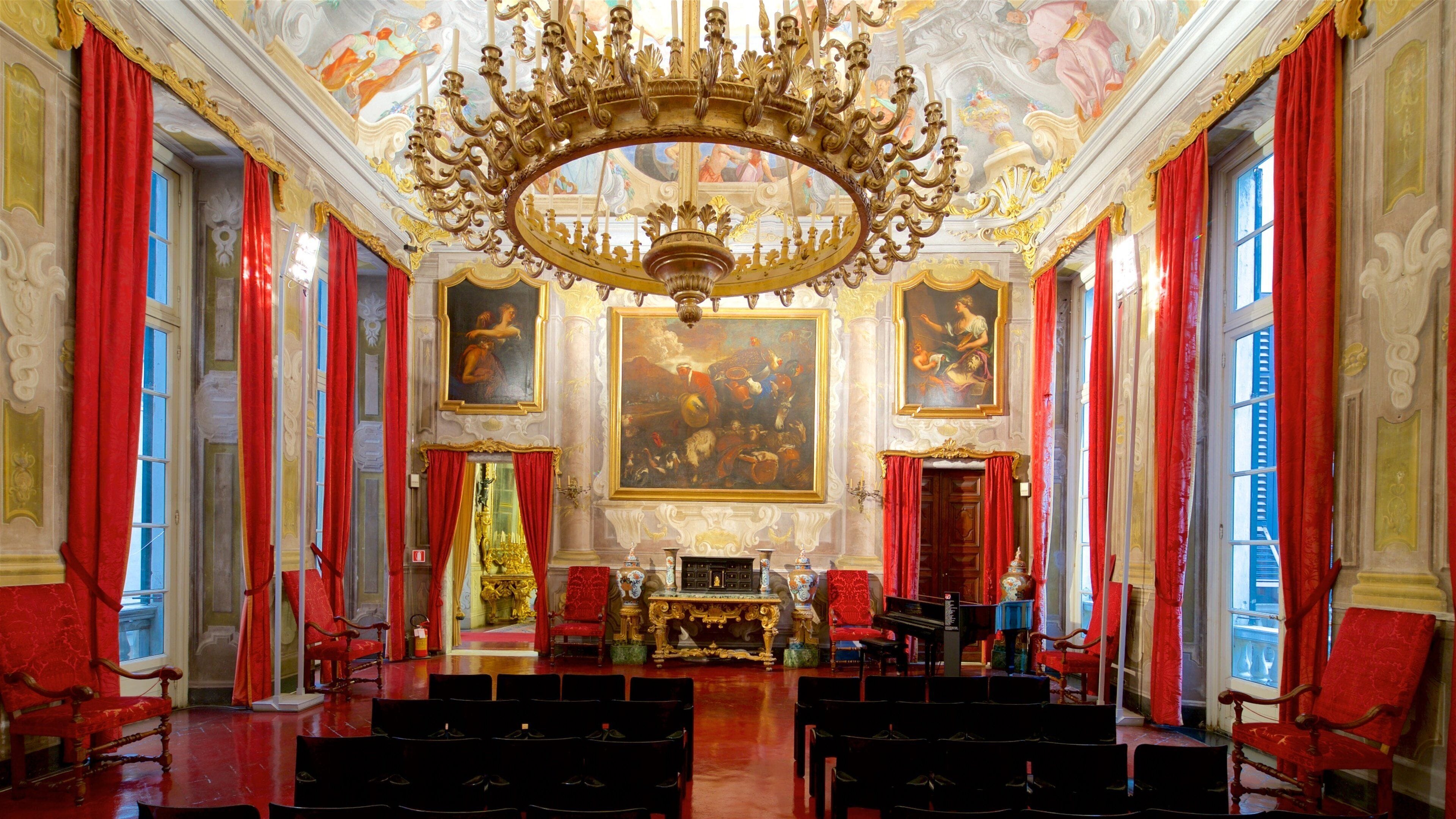 A grand hall with ornate chandeliers, red curtains, and classical paintings.