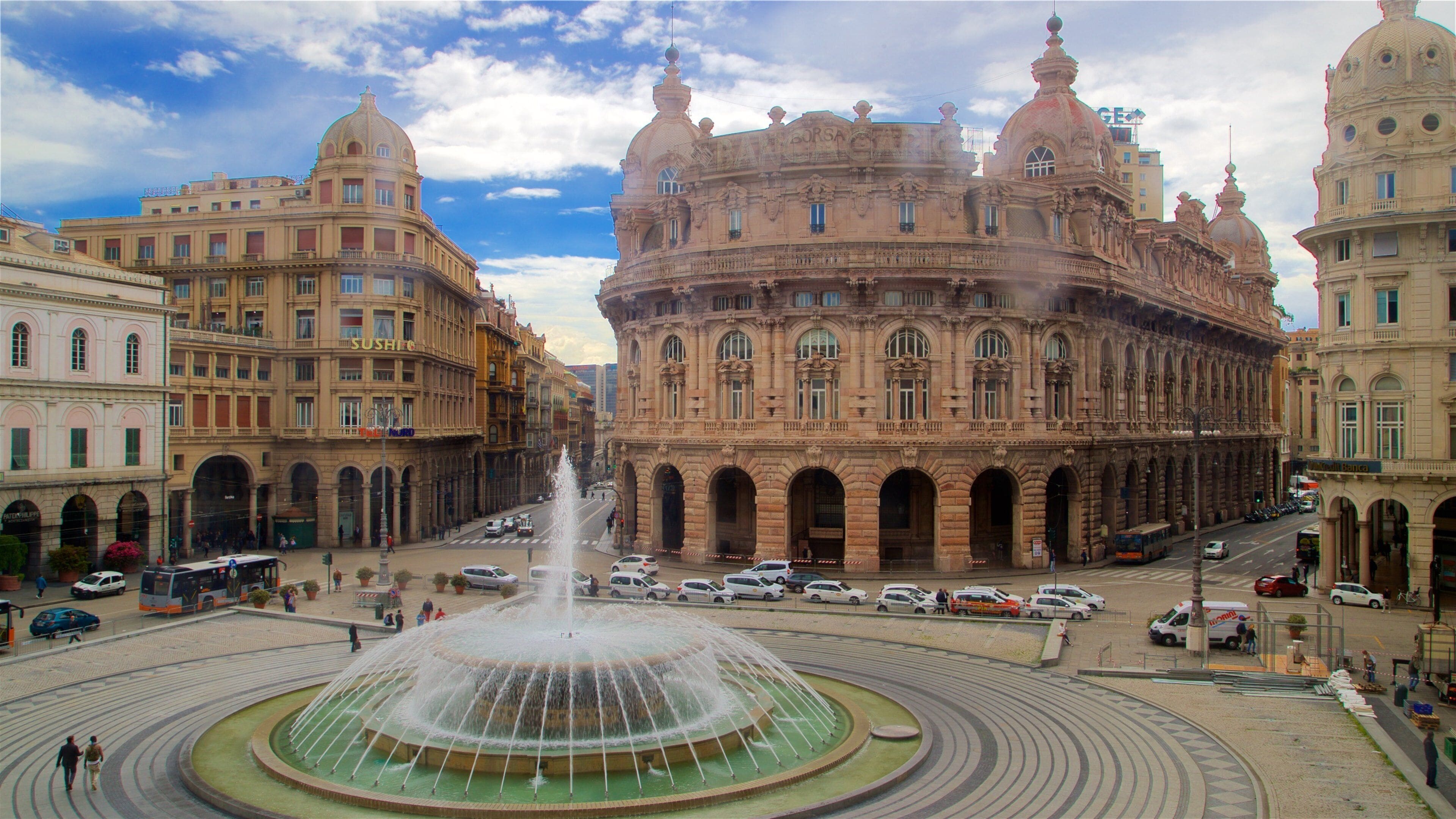 A historic building with ornate architecture, a central fountain, and surrounding streets with cars and pedestrians.