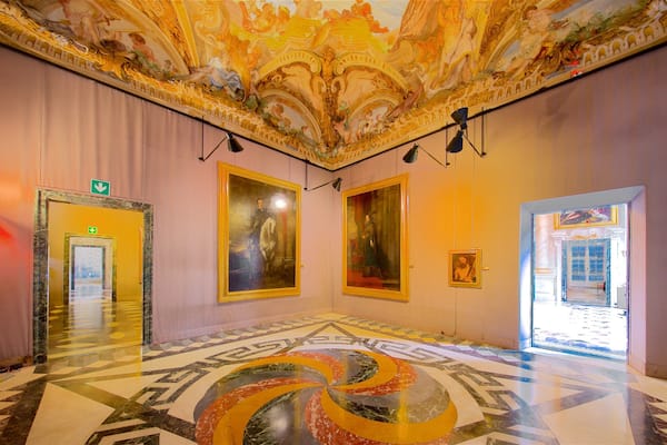 Un vaste hall d’entrée orné de fresques au plafond, de grands tableaux encadrés et d’un sol à motifs.