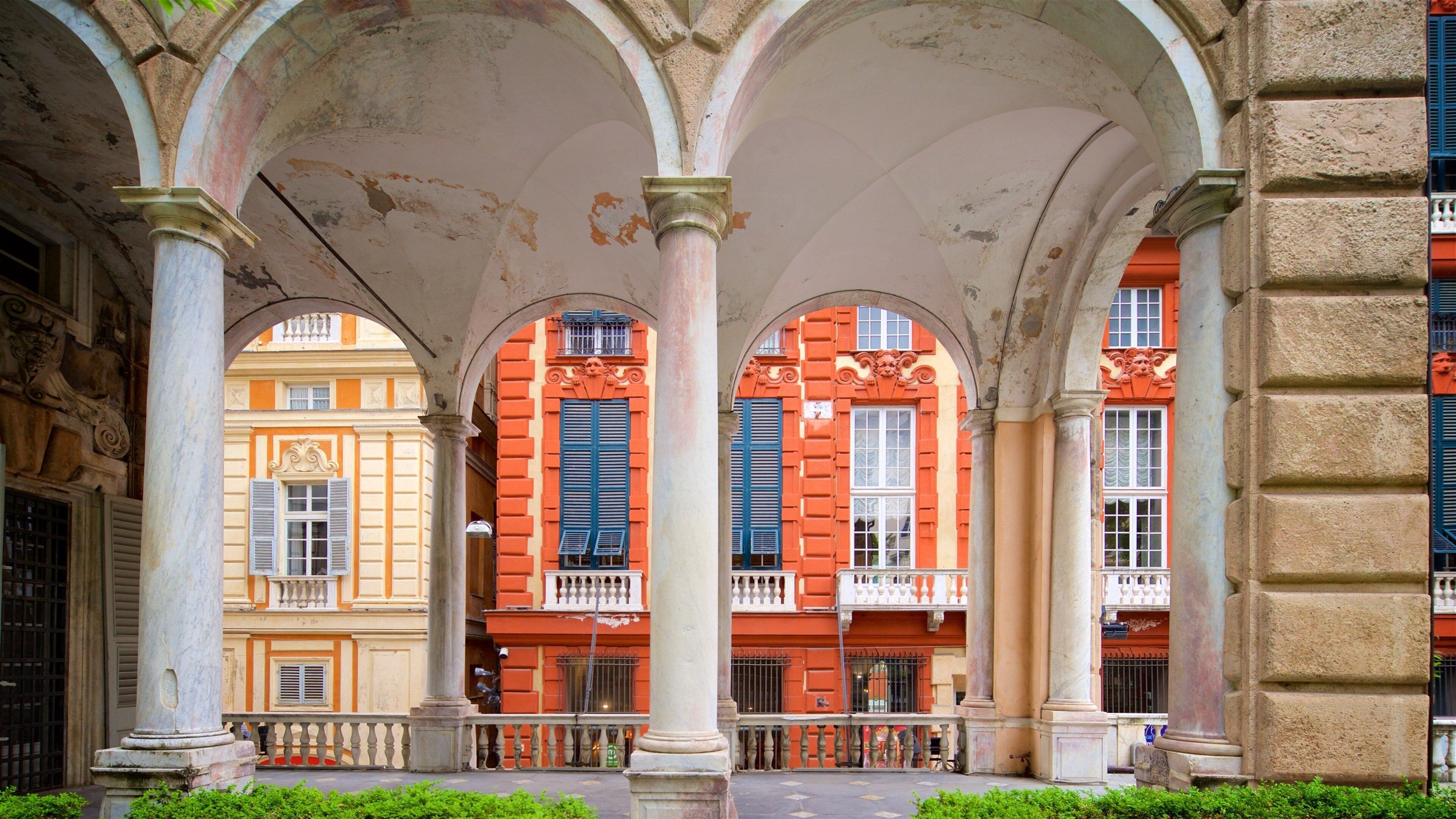 Une zone piétonne abritée, agrémentée d’arcades, de colonnes et de bâtiments aux façades rouges et jaunes.