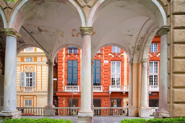 A covered pedestrian area with arches, columns, and buildings with red and yellow facades.