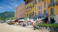 Ett livligt torg med färgglada byggnader, uteserveringar och en imponerande bergskuliss i bakgrunden.