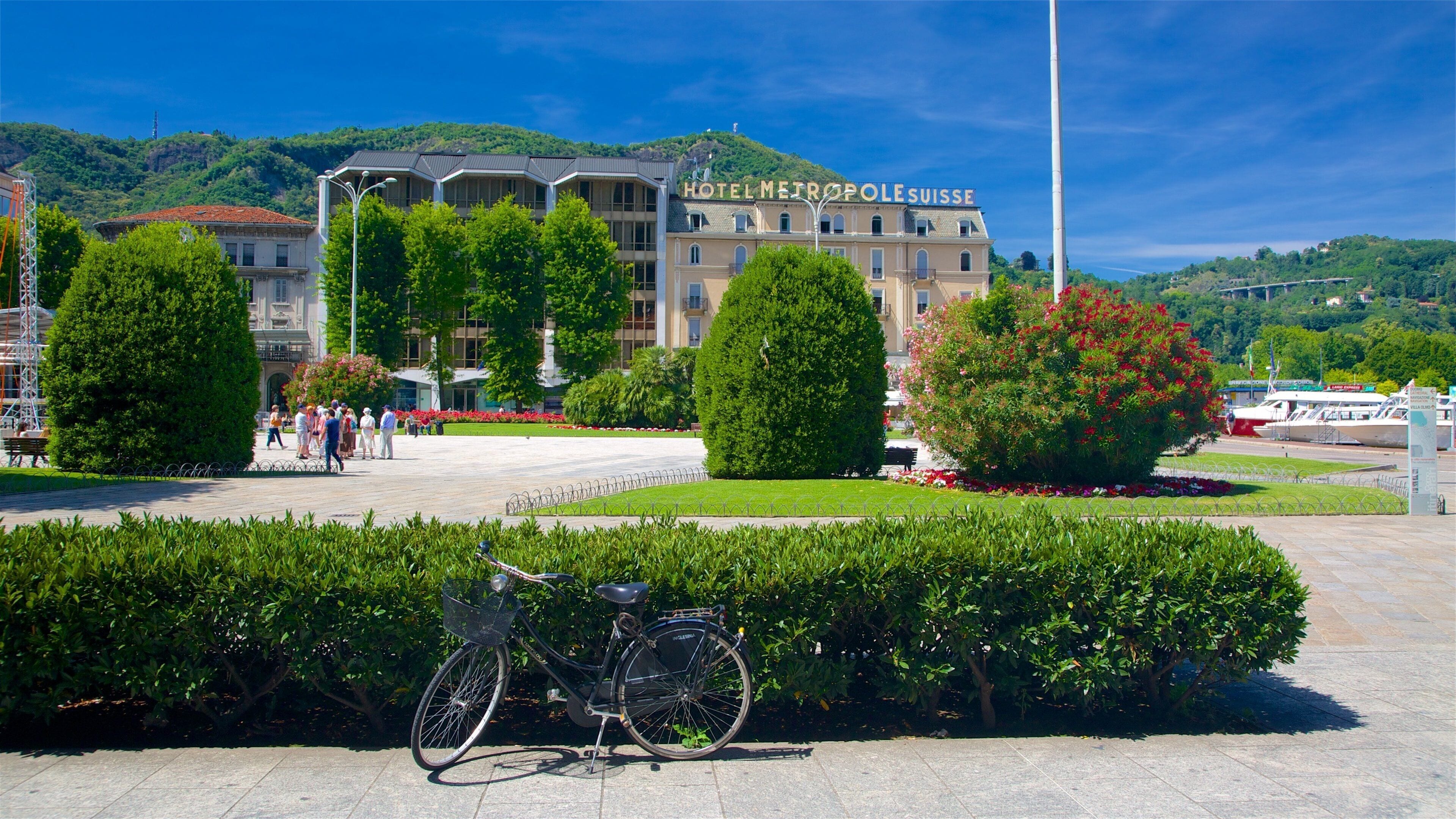 Hotelli nimeltä ”HOTEL METROPOLÉ SUISSE”, jonka taustalla kohoaa vuoristo, ja jonka yhteydessä on pyörä ja hyvin hoidettu puutarha.