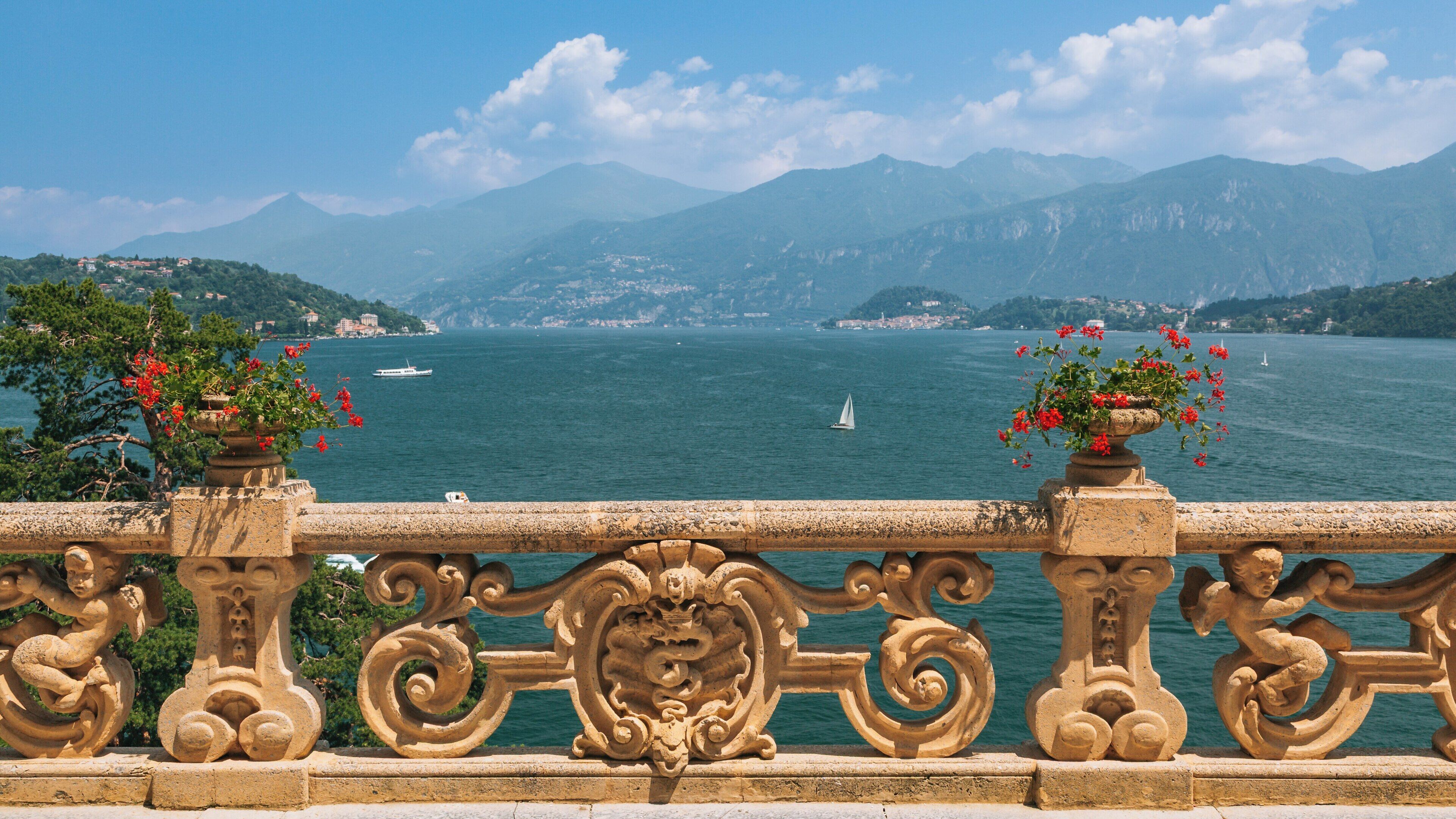 Villa del Balbianello offers stunning views of Lake Como surrounded by lush mountains and vibrant flowers in Lenno, Lombardy, Italy on a clear sunny day