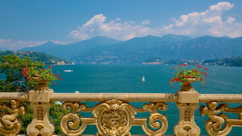 A scenic view of a lake with mountains in the background, a boat, and ornate balustrades with flowers.