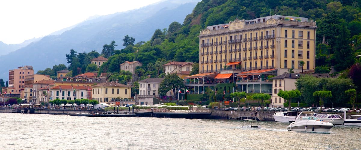 A coastal town with historic buildings, a marina, and mountains in the background.