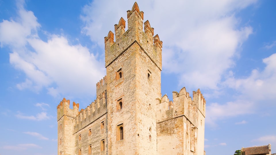 Un castello storico in pietra, con merli e una torre, sotto un cielo sereno.