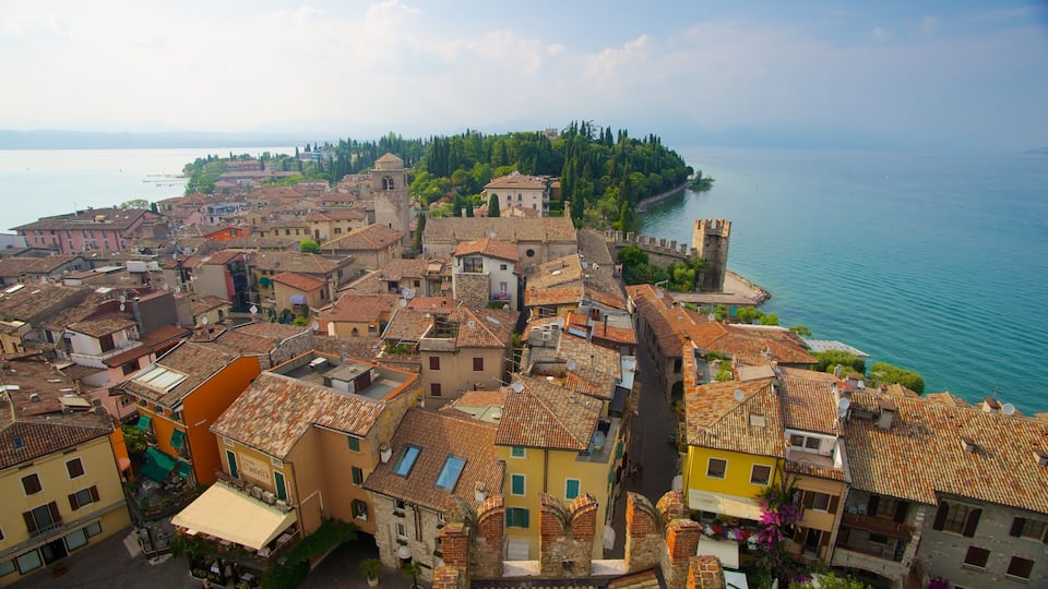 Una cittadina costiera con edifici dalle tegole color terracotta, una torre imponente e un’isola alberata sullo sfondo.