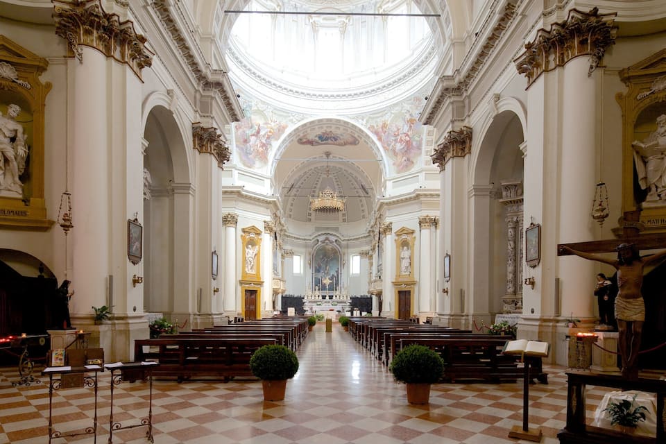 Eine Kircheninnenansicht mit hoher Decke, aufwendiger Dekoration und einem Schachbrettmuster-Boden.