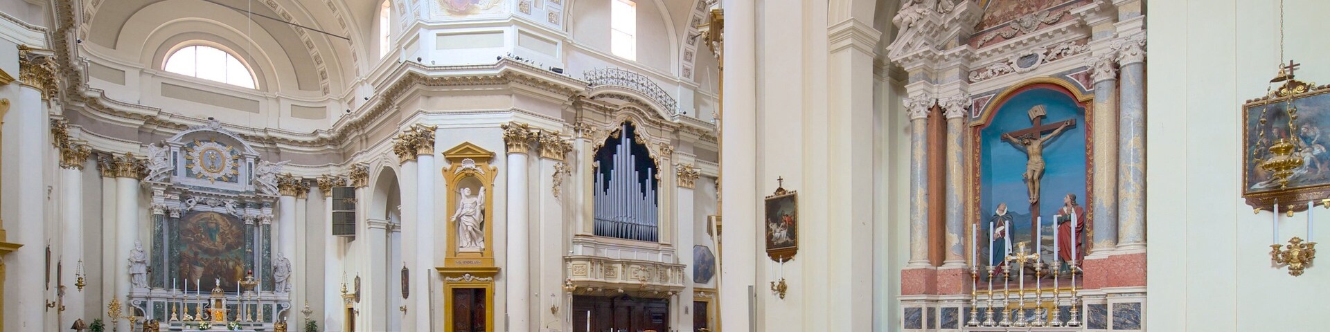 An ornate church interior with wooden pews, a large organ, and a crucifix.