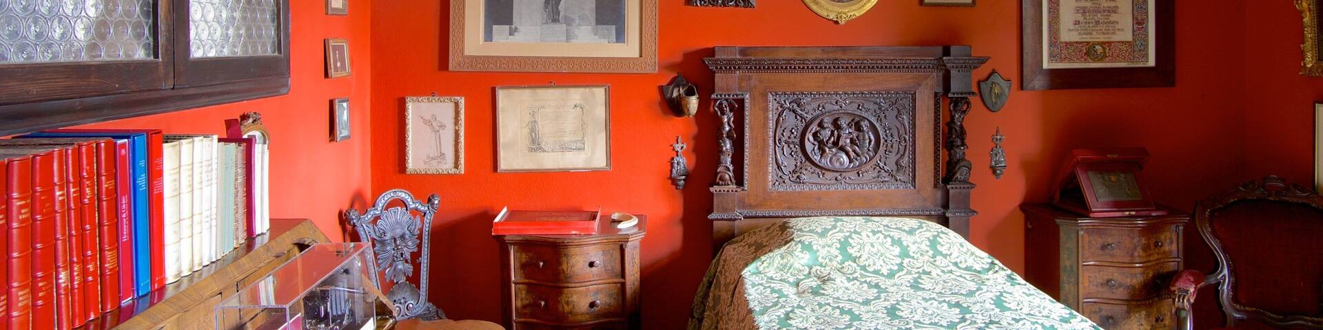 Una habitación con pared roja, muebles de madera y varias fotos y objetos enmarcados.
