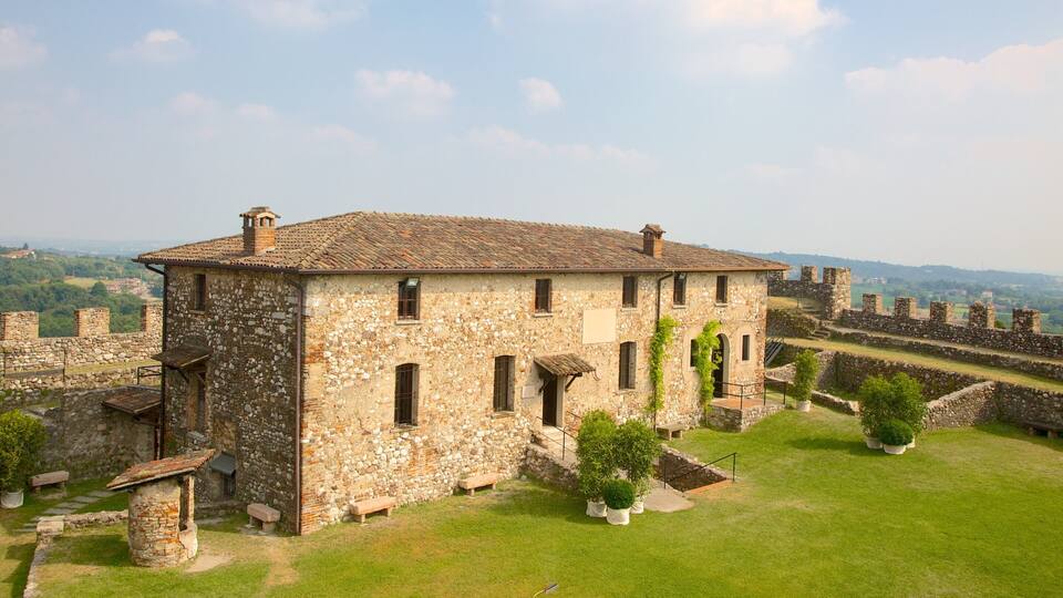 A stone building with a tiled roof surrounded by a stone wall and a grassy area with potted plants.