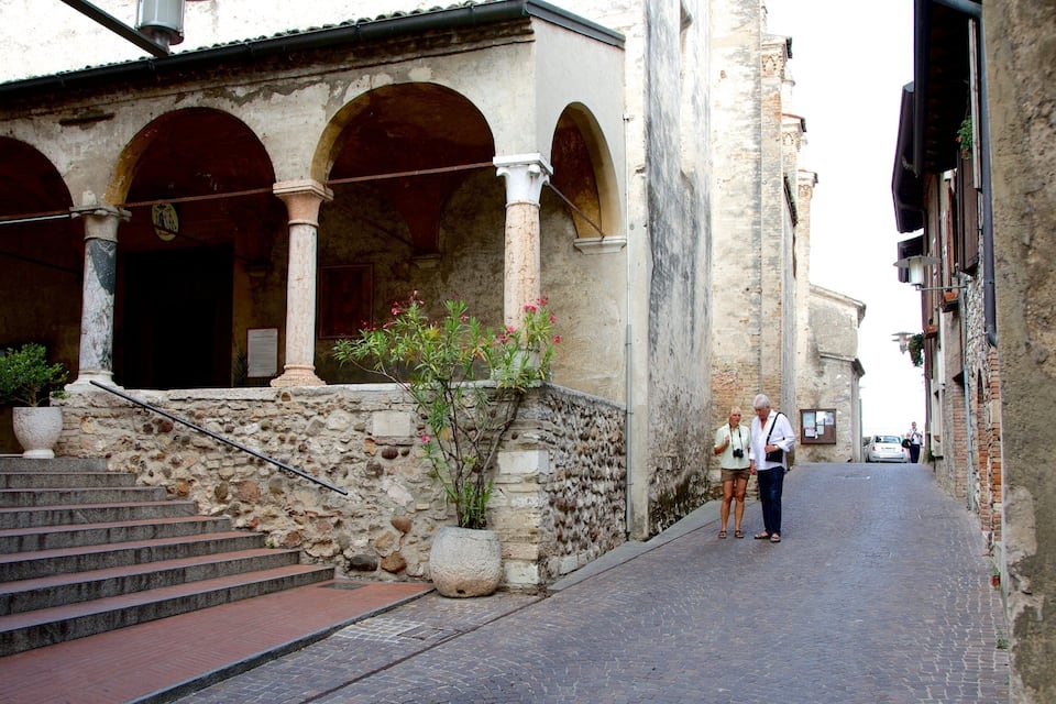 Une ruelle étroite pavée, bordée de bâtiments historiques en pierre, dotés d’arcades et d’un escalier menant à un niveau supérieur.