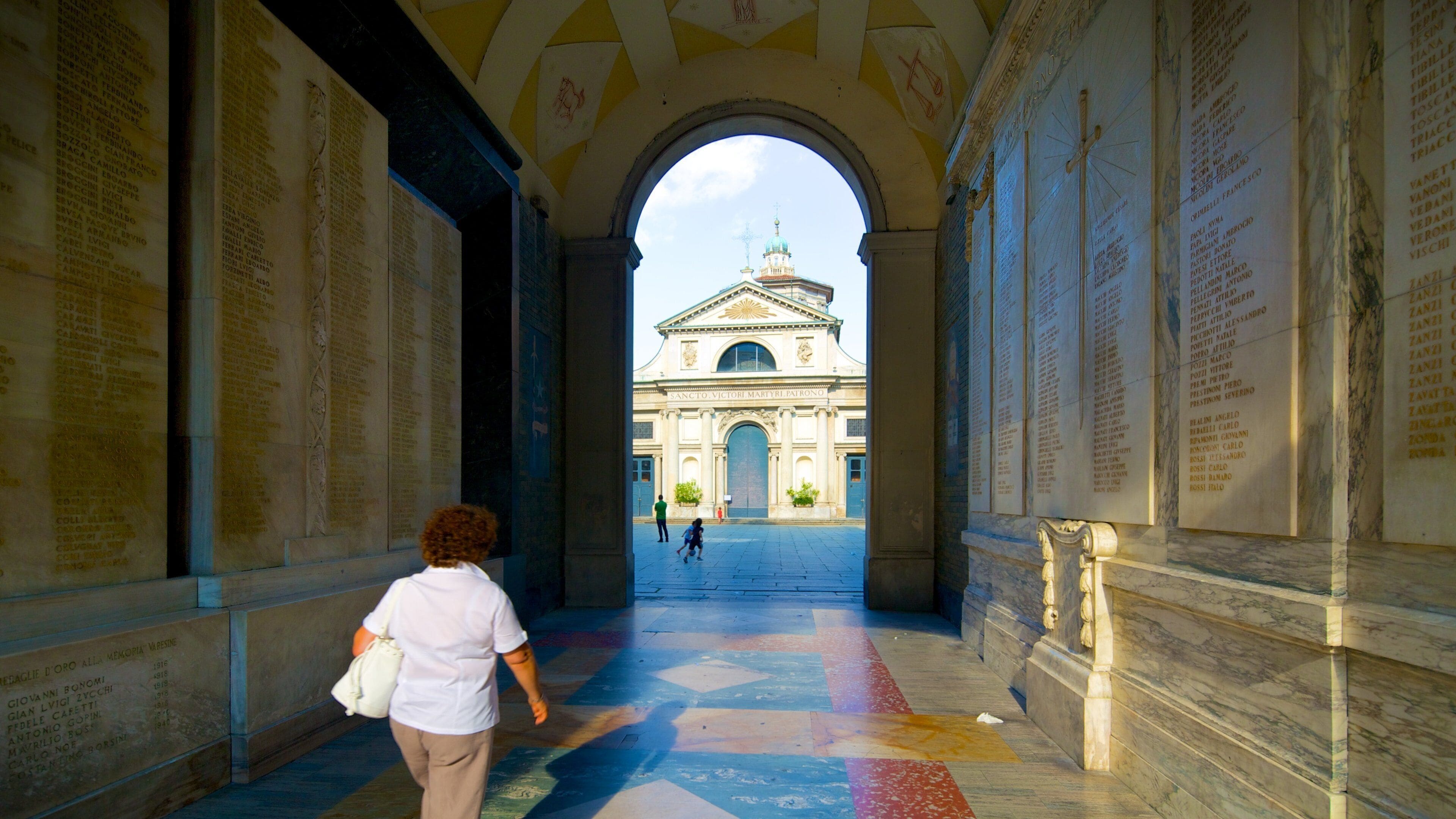 A marble corridor with inscriptions, leading to a grand building with a dome.