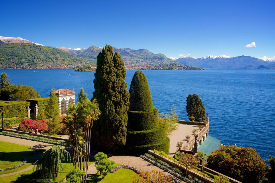 A lake with mountains in the background, a well-maintained garden with various plants, and a small building with a red roof.