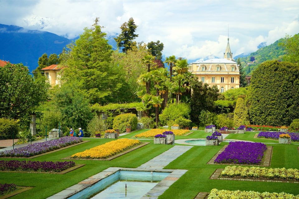 A well-manicured garden with various flower beds, a fountain, and a large building with a spire in the background.