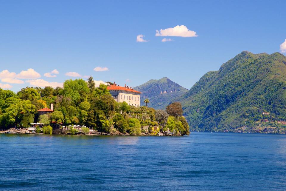 A lake with a house on a small island, surrounded by lush green hills.